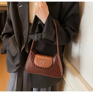 Détail de la texture cuir de crocodile marron foncé et boucle nœud argenté du sac à main