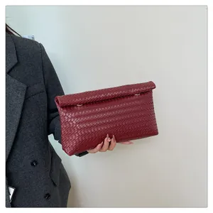 Detailed texture of burgundy woven leather clutch bag with elegant gold metal fasteners