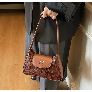 Détail du sac marron avec motif crocodile et ornement de nœud en métal doré