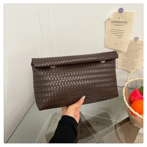 Close-up of deep brown woven leather clutch with gold round metal accents on a glass table