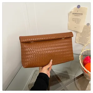 Close-up of brown hand-woven leather envelope clutch with intricate intrecciato weave pattern