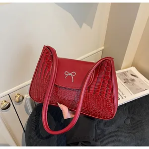 Détail du sac à épaule rouge avec texture crocodile et nœud métallique argenté