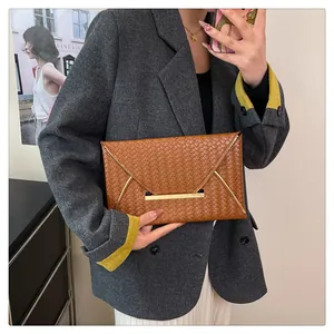 Détail d'une pochette tressée marron avec fermoir en métal doré sur un costume gris
