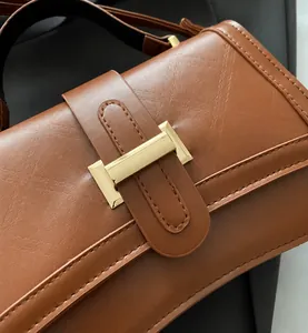 Close-up of brown textured leather handbag featuring a golden H-shaped metal buckle detail