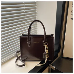 Détail du cabas en cuir verni marron foncé avec chaîne décorative et logo de marque