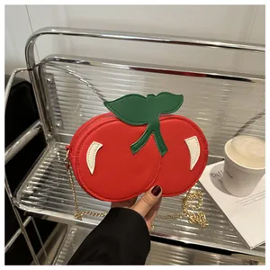 Detalle de bolso bandolera rojo en forma de cereza con hoja verde y cadena dorada