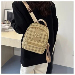 Detailed macro view of the beige letter-patterned fabric and golden metal M-logo on backpack