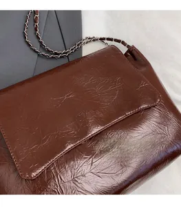 Detail of dark brown glossy leather tote with FASHIONBAGS embossing and chain strap