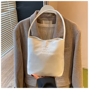 Detail der weißen Satin-Beuteltasche mit Hope and future Stickerei auf braunem Blazer