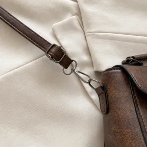 Detail van donkerbruine leren tas met lychee-textuur en houtskoolkleurige metalen haak-sluiting