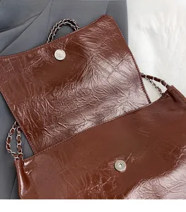Detail of silver magnetic buckle and chain strap on a dark brown leather shoulder bag