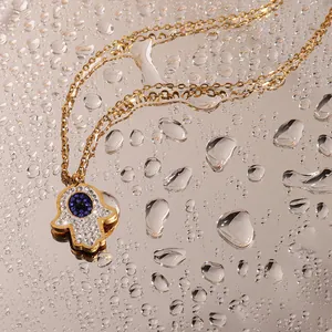 Close-up of golden Hamsa Hand pendant with blue Evil Eye and pavé diamonds on water drops