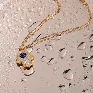 Macro detail of Hamsa Hand pendant with blue stone and crystals on golden chain with water drops