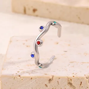 Irregular wavy silver titanium steel ring with colorful rhinestones on a stone background