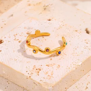 Detail of wavy gold titanium steel ring featuring colorful inlaid stones on a stone base