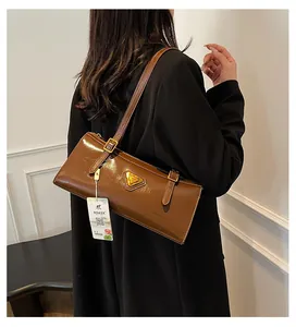 Detailaufnahme der braunen Ölwachs-Ledertasche mit goldenem Dreieck-Metall-Logo am Gurt