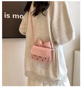 Détail d'un sac bandoulière rose avec un grand nœud et des pois noirs sur cuir brillant