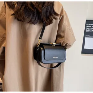 Detail of black matte leather crossbody bag with white text print on a khaki coat