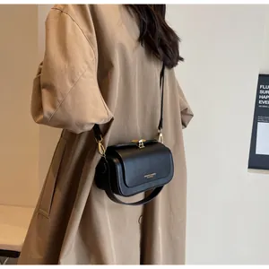 Detail of minimalist black leather crossbody bag with gold metal hardware and flap closure