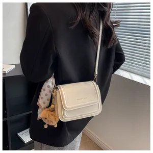 Schicke beige Umhängetasche mit Seidenschal und Plüsch-Anhänger auf schwarzem Anzug