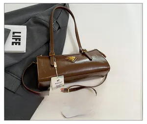 Detail der dunkelbraunen zylindrischen Schultertasche mit goldenem Logo und Lederstruktur