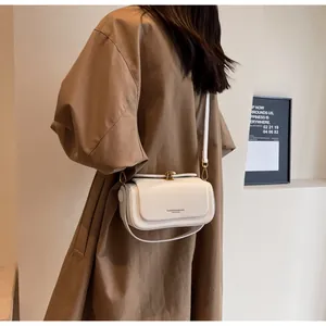 Detail of white leather crossbody bag with gold hardware worn over a brown trench coat
