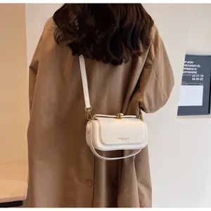 Detail view of white leather crossbody bag featuring gold hardware and logo on model
