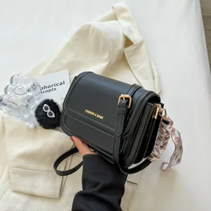 Minimalistische schwarze Umhängetasche mit Goldlogo, Seidentuch und Plüschanhänger