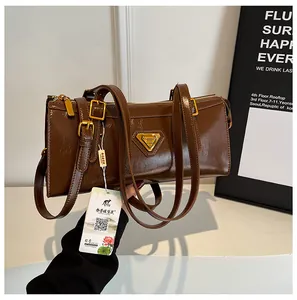 Details einer braunen, glänzenden Lederhandtasche mit goldenem Logo und Trageriemen