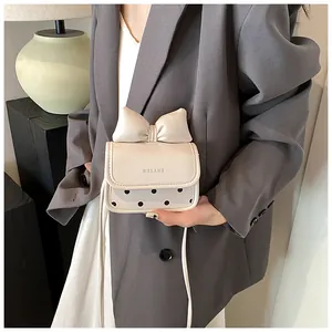 Détail du mini sac crème avec nœud 3D, pois noirs et logo HELAHE embossé sur le rabat