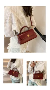 Detail of burgundy patent leather handbag featuring a golden square clasp and adjustable strap