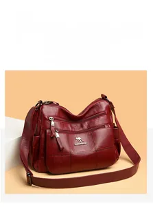 Detail of burgundy lychee grain leather crossbody bag with multiple zip pockets and strap