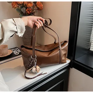 Close-up of brown oil wax leather tote bag featuring a baseball charm and glossy finish