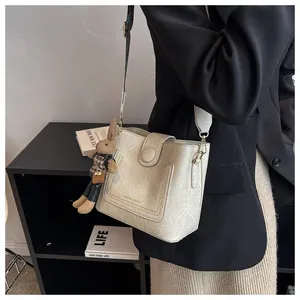 Détail d'un sac seau beige avec bandoulière réglable et breloque lapin en peluche