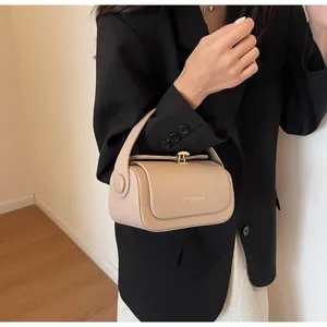 Detailed view of cream cylindrical bucket bag with gold metal buckle on a black suit