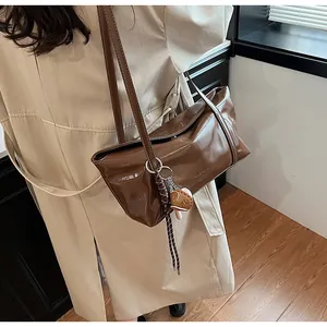 Detail of a brown glossy leather shoulder bag with CLEARON logo and creative charm