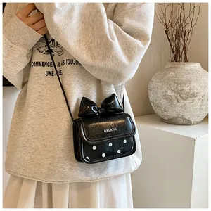 Détail d'un mini sac bandoulière avec nœud noir et motif à pois blancs sur cuir synthétique