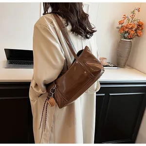 Detail of dark brown oil wax leather shoulder bag featuring a side woven charm and logo