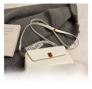 Detail view of white square bag with golden lock and adjustable strap on wool coat