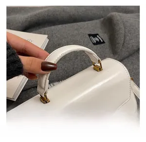 Detail of a white leather handbag featuring a sturdy handle and gold metal hardware