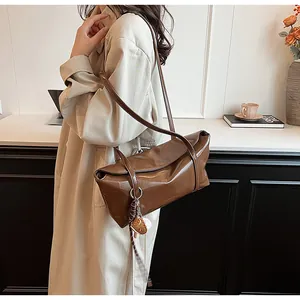 Close-up of brown polished leather shoulder bag with decorative charm on trench coat