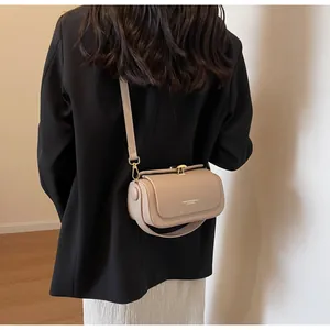 Detail showing the beige leather crossbody bag with a gold metal clasp and adjustable strap