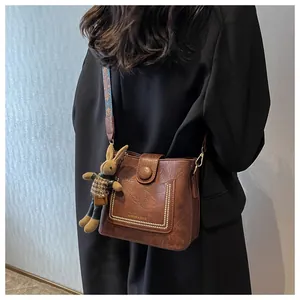 Détail du sac seau vintage en cuir PU marron avec rabat à rivets et sangle jacquard colorée