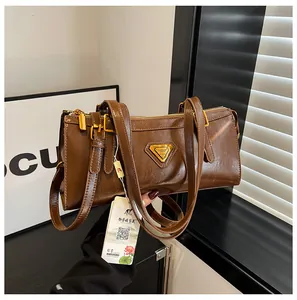 Detailaufnahme der braunen Leder-Schultertasche mit goldenen Beschlägen und Dreieckslogo