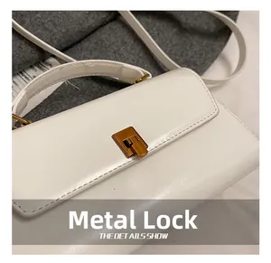Detailed macro view of the golden rectangular hardware clasp on a white leather handbag