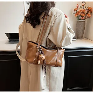 Detail of a brown oil-wax leather shoulder bag with a stylish spherical charm and tassel