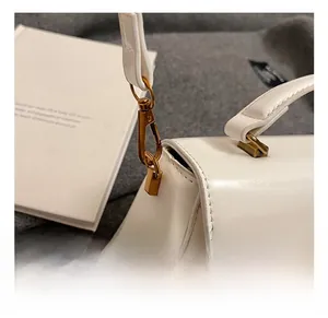 Close-up of premium gold-toned metal hook and white leather strap on a stylish handbag