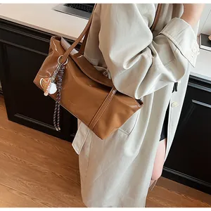 Detailed shot of caramel oil wax leather shoulder bag with baseball charm on beige trench coat