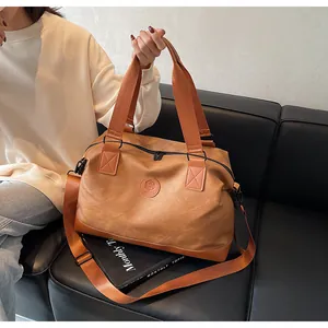 Détail du sac de voyage caramel montrant le logo rond gaufré et la large poignée