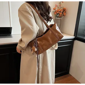 Detail of a brown oil wax leather shoulder bag with a fish charm on a beige trench coat